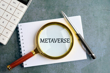 Metaverse concept. Written metaverse single word through a magnifying glass on a notebook in a composition with a calculator, a pen on a gray background