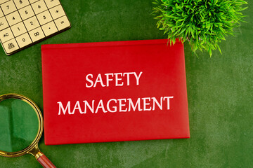 Safety Management text written on the cover of a business notebook on a beautiful green background with a calculator, magnifying glass and a plant