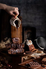 Chocolate brownie cake with cream sauce on table with chocolate bar ingredients and kitchen utensils
