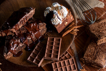 Chocolate brownie cake with cream sauce on table with chocolate bar ingredients and kitchen utensils