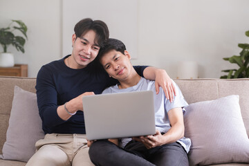 Fototapeta premium A gay couple spends their free time sitting on a laptop doing activities together on a holiday in the living room.