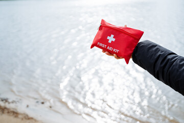 A beachgoer is carrying a red first aid kit by the water