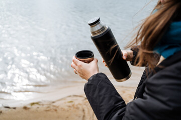 Woman by the beach with cup and thermos, enjoying winter landscape
