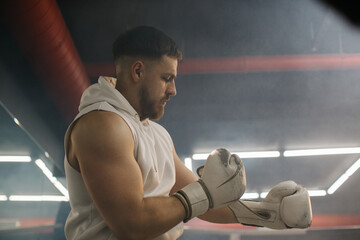 A male boxer puts on gloves on the background of a ring in a boxing club.