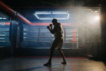 A male boxer is boxing with a shadow on the background of a boxing ring. A boxer practices his...