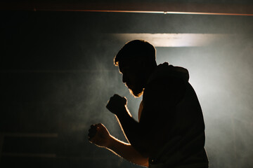 A male boxer is boxing with a shadow on the background of a boxing ring. A boxer practices his...