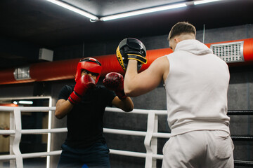 Training inside the boxing ring. A teenage boxer in boxing gloves practices punches with his trainer.