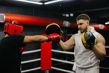 A teenager wearing a red protective helmet and gloves trains in a boxing ring with a coach.