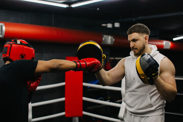 A teenager wearing a red protective helmet and gloves trains in a boxing ring with a coach.