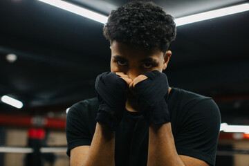 A determined young boxer is looking at the camera while standing in a fighting stance with boxing...