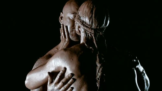 Amid the darkness on a black background, an amazing story of passion and devotion is spilled, where a man with a strong physique and his gorgeous wife, covered in clay