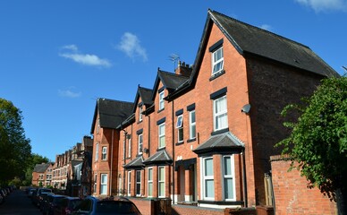 a typical English small town street with narrow terraced, adjoining red brick houses with bay windows