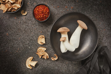 King Oyster mushrooms or Eringi in a bowl and dried white mushrooms on a dark background. Flat lay.