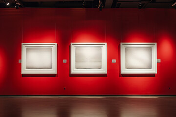 Gallery display: three white frames mounted on a red wall, each under a strategic spotlight.