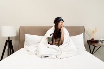 Woman Yawning In Bed With Eye Mask And Coffee Mug, Depicting A Cozy Morning Routine. Warm, Comfortable Bedroom Setting, Capturing Everyday Lifestyle And Relaxation.