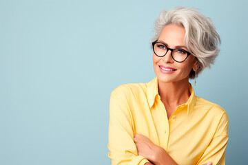 Portrait of a beautiful business elderly woman with short gray hair wearing glasses and a yellow blouse on a blue background, copy space