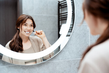 Happy Young Woman Brushing Teeth In Modern Bathroom, Reflecting In Mirror With Elegant Interior....