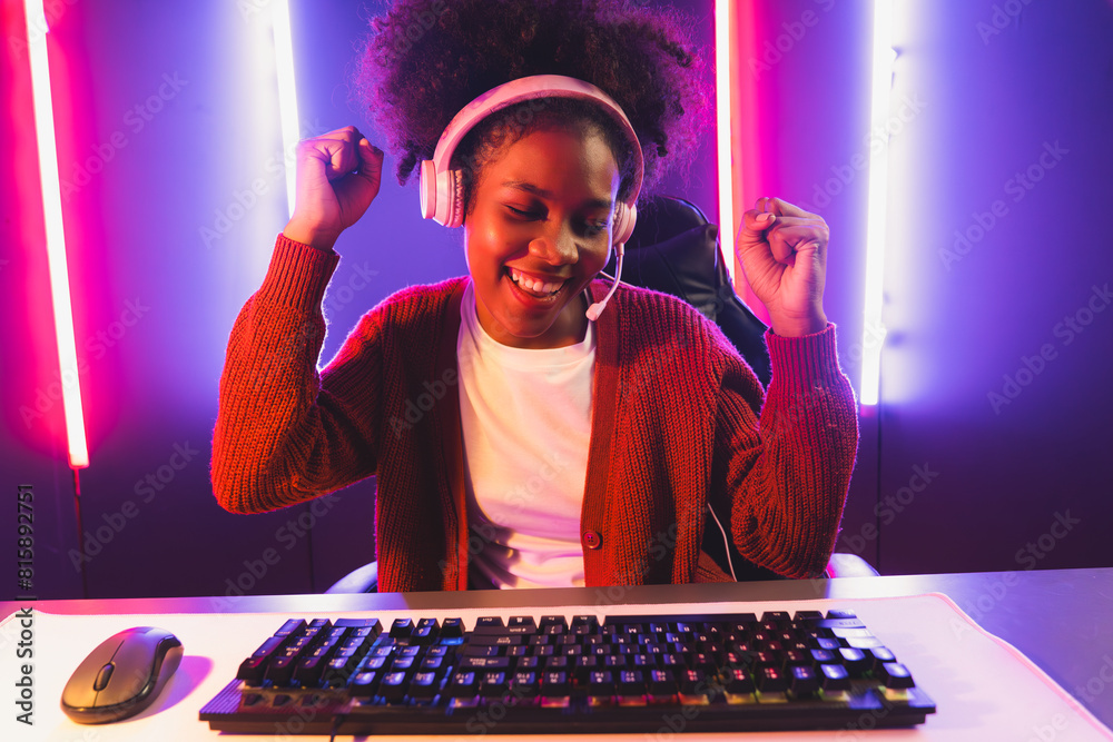 Wall mural Gaming streamer, African girl playing online fighting with Esport skilled team wearing headphones in neon color lighting room. Talking other players planing strategies to win competitors. Tastemaker.