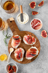 Bruschetta or toast with goat cheese spread, prosciutto, figs and honey on a board.