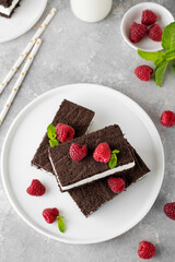 Chocolate cake with milk cream filling on a white plate with fresh raspberries and mint with bottles of milk. Delicious dessert. Copy space.