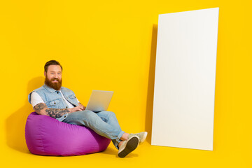 Photo of cute funny man wear jeans waistcoat sitting beanbag typing modern device empty space...