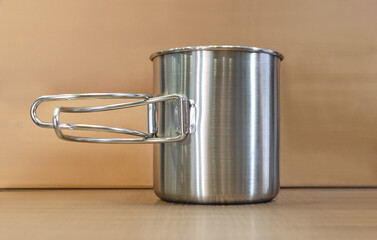 Iron cup on the table. Silver metallic travel cup, brown background. Leisure and travel concept.