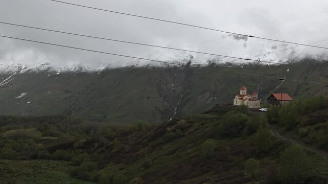 Gudauri, Georgia in cloudy weather with green grass and snow on montains pics in May. View on Orthodox church.