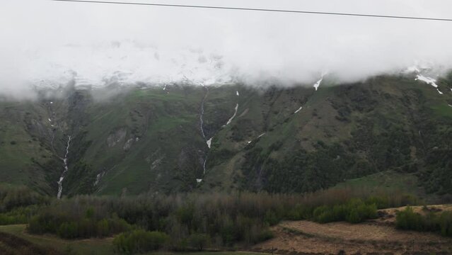 Gudauri, Georgia in cloudy weather with green grass and snow on montains pics in May. View on Orthodox church.