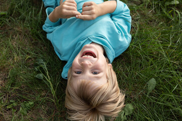 close-up of the face of a cute cheerful boy lying on the green grass, top view. enjoying nature outdoors. dreaming in the park. Spring, summer, outdoor recreatio