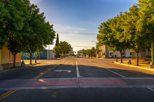 Fresno, California, USA - June 17, 2023 : Sunlit, quiet morning on Van Ness Avenue in Downtown Fresno, California, showcasing an empty street flanked by green trees and a colorful mural.