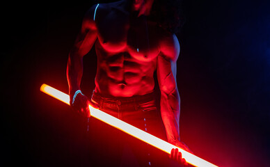 Muscular strong guy with naked torso abs holds neon light tube in dark room