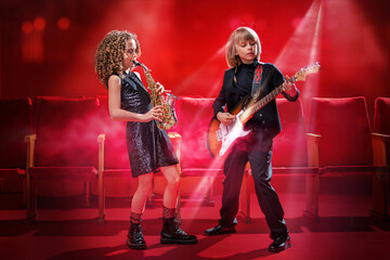 Two young children playing music together, one on a saxophone and the other on a guitar.