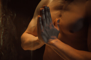 Praying sporty muscular man holding namaste palms gesture under colorful illumination, laser light