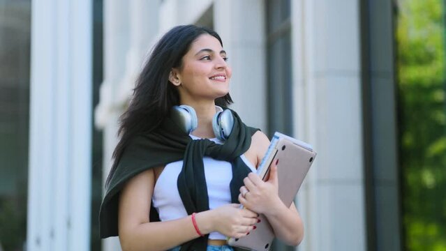 Beautiful brunette indian girl student with notebooks walking down at urban city street after lessons in university and looking around outdoors Successful student concept. High quality 4k footage