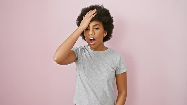 Black, curly african american woman in t-shirt, standing clueless with hand on head, annoying memory error. regretting foolish blunder, forgot something important. isolated on pink background.