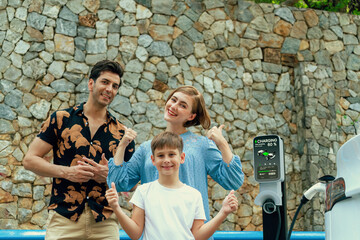 Fototapeta premium Family road trip vacation with electric vehicle, lovely family recharge EV car with green and clean energy. Stone seawall background and eco friendly car travel for sustainable environment. Perpetual