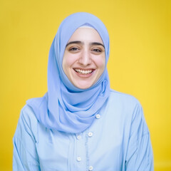 Smiling Muslim woman in blue hijab on yellow background
