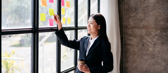 A woman in a business suit is writing on a whiteboard with yellow