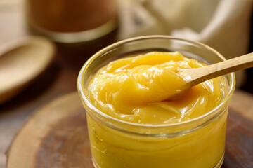 Ghee butter in glass jar with wooden spoon on wooden table with blurred background.