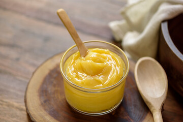 Ghee butter in glass jar with wooden spoon on wooden table with blurred background.