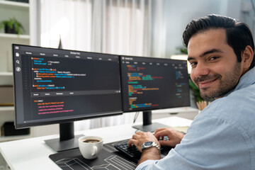 Smiling smart IT developer working software development looking camera with coding on two pc...