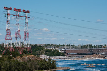 Hydroelectric power station by a river with high voltage power lines and rocky shores, showcasing...