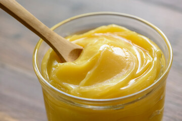 Ghee butter in glass jar with wooden spoon on wooden table with blurred background.