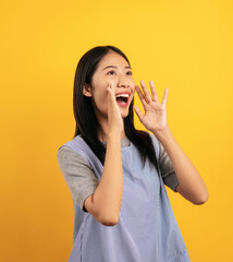 Young asian woman in casual clothes putting hands near mouth to screaming and shouting announcing...