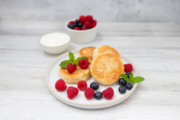 Cottage cheese pancake or syrniki with fresh raspberries and blueberry on white wooden table.  Sweet breakfast or lunch, tasty dessert. 