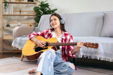 Young woman is playing guitar and singing the song while wearing headphone to listening music and...