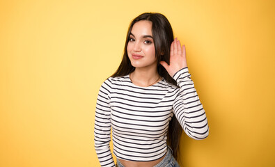 Young woman listening to something on a yellow background