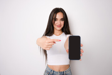 Smiling young woman showing empty smartphone screen and pointing isolated on white background.