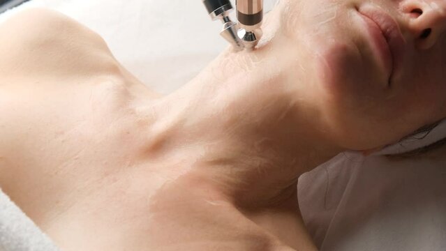 A woman undergoes a microcurrent procedure from a cosmetologist, close-up of her neck.