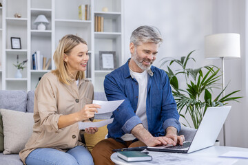 Mature couple managing their finances and documents while working together on a laptop at home.